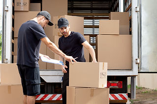 Two workers in black uniforms and caps organize cardboard boxes at the back of a truck