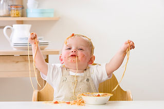 Messy baby boy in high chair eating spaghetti