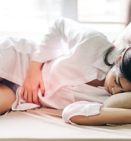 A woman resting on the couch, holding her stomach, experiencing menopause pain