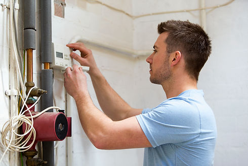 Repairman in a blue shirt fixing a domestic heating system and red circulation pump in a new home