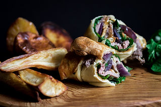 A steak sandwich cut in half with onions and greens