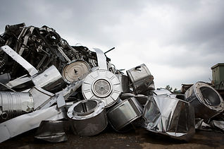 Discarded washing machine drums and metal debris under a cloudy sky.