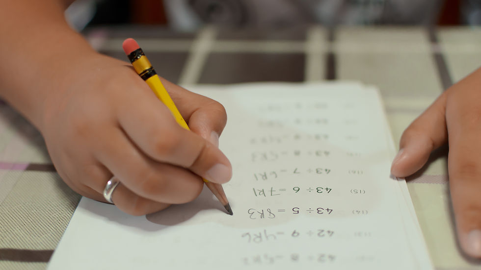 Hands holding a pencil, writing math equations on paper. Soft focus, plaid tablecloth background, educational theme.