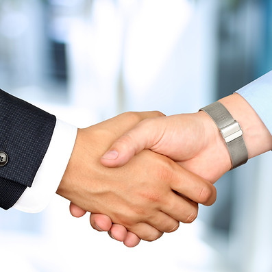 Two people shaking hands, one in a dark suit and the other in a light shirt with a bracelet.