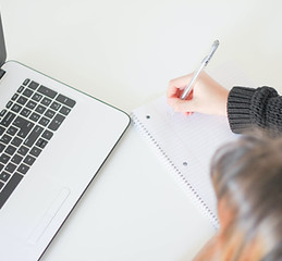 Girl taking note next to a laptop