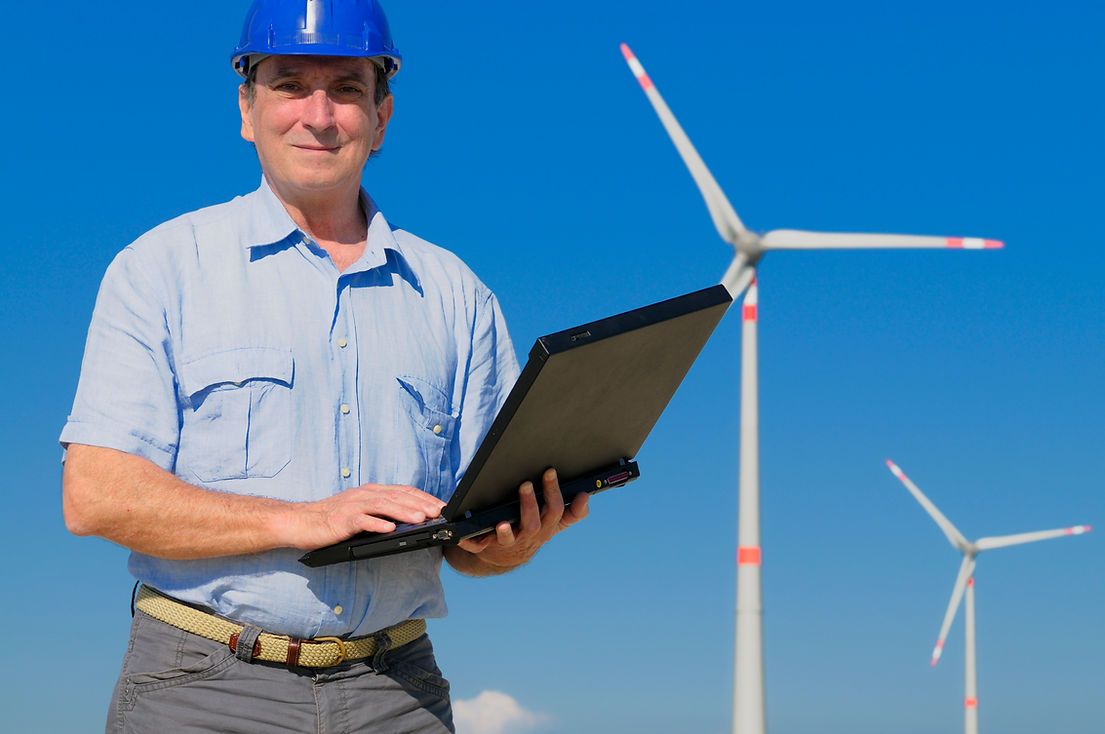 Renewable energy engineer with laptop standing in front of two wind turbines
