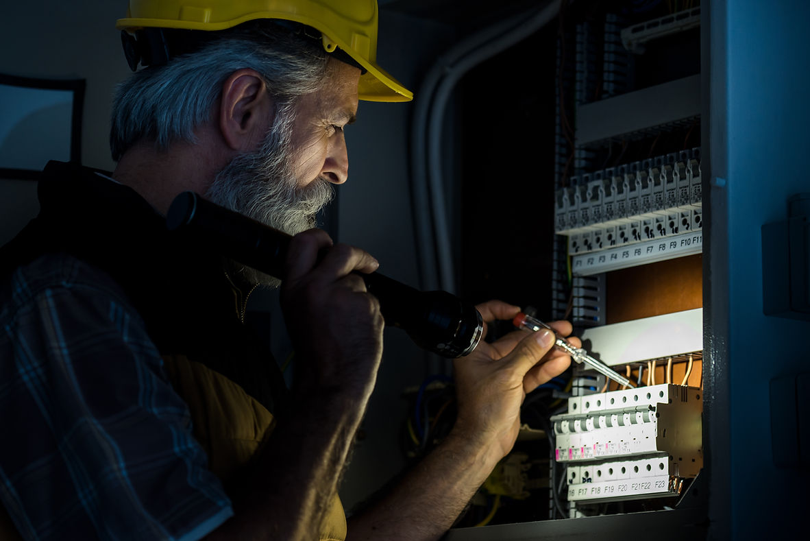 An electrician working on an electrical panel, using a flashlight and screwdriver