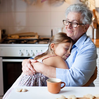 Una abuela abrazando a su nieta mientras toma un café con dulces. Es una imagen positiva de la vejez
