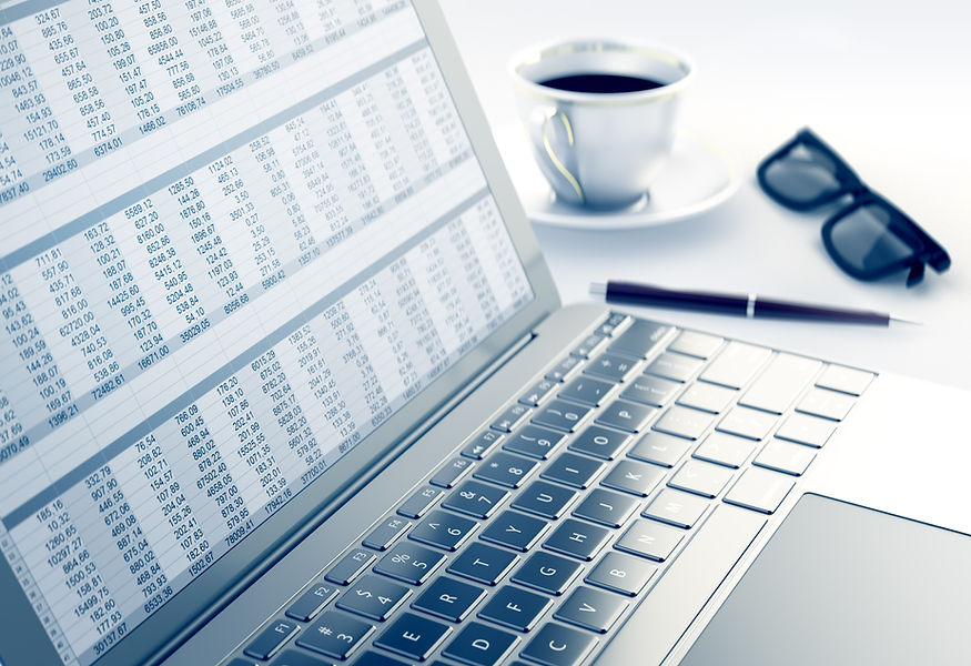 Close-up of a modern computer keyboard next to blurred spreadsheet numbers and glasses