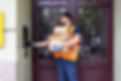 A delivery person holds several packages while pressing a doorbell