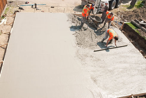 A group of workers is pouring concrete on a large slab, focused on their tasks in a construction site setting