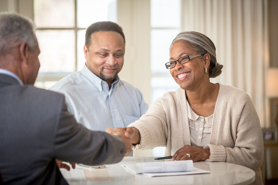 A smiling woman in a cardigan shakes hands with a man in a suit across a table