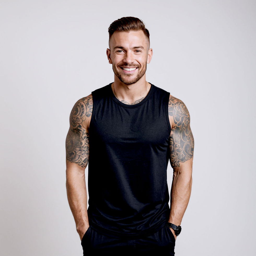 Smiling man with tattoos wearing black tank top, sports shoes, studio shot.