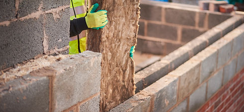 A man wearing yellow gloves holds a brick in his hands, ready to use it for construction