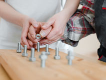 Someone helping another individual screw a nut onto a bolt.