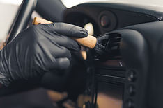 Close-up of gloved hand inside car brushing the air vents on dashboard. Precision work.