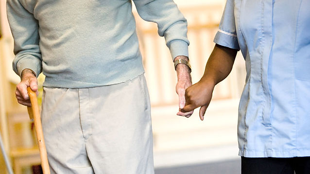 Elderly man walking with the aid of a carer