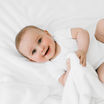 A happy baby laying on his back on a white bed.