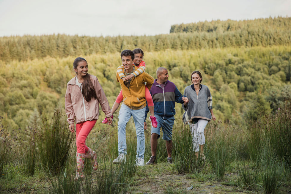 Family hiking through a forest with a young girl piggybacking on a boy