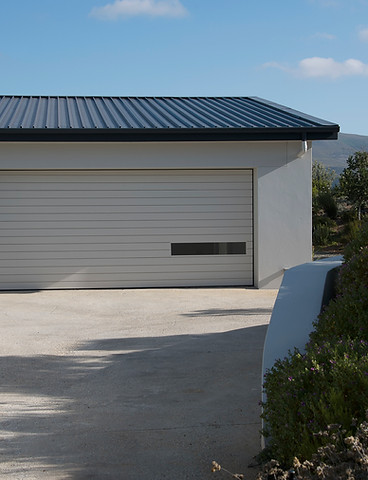 Clean concrete driveway leading to a modern residential white garage with a black roof