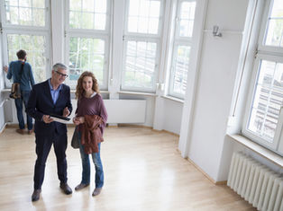 Zwei Menschen stehen in einem leeren Raum mit großen Fenstern.