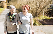 Full length of senior woman with female home caregiver walking arm in arm on street