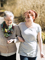 Female home caregiver walking in arms with elderly women