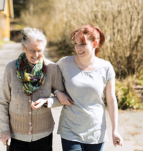 Full length of senior woman with female home caregiver walking arm in arm on street