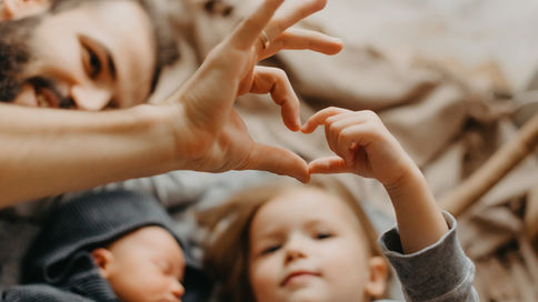 Dad making a heart symbol with his daughter as a newborn is sleeping peacefully.