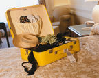 Open yellow suitcase with summer clothes on a hotel bed