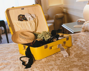 Open yellow suitcase with summer clothes on a hotel bed