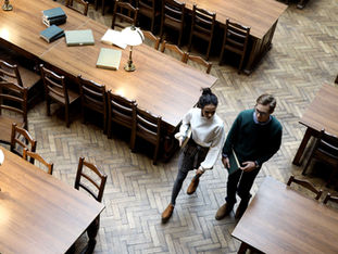 Two students walking in a library.