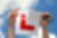 Close-up image of a person's hand holding a partially torn L-plate, with a blue sky in the background