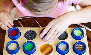 A child in a pink shirt plays with a tactile board featuring various textured circles