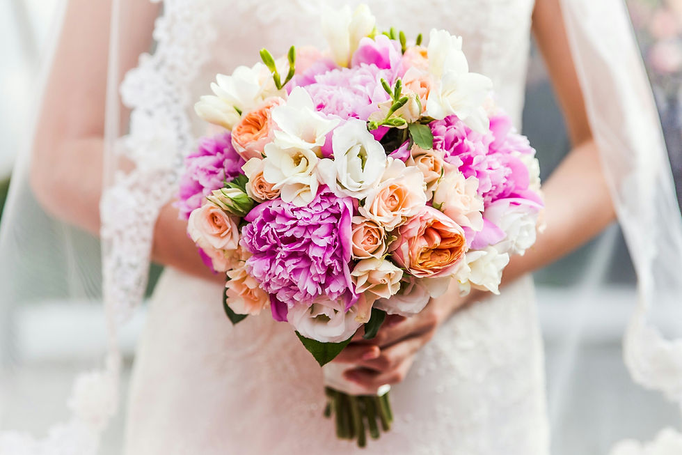 A bride holds a vibrant bouquet of pink, peach, and white flowers
