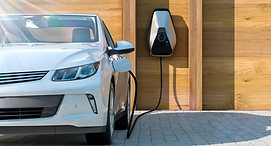 A white electric car is connected to a charging station, indicating it is being charged