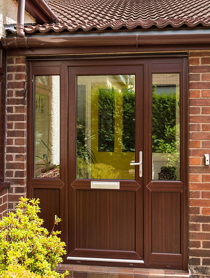 Dark wood front door and glazed porch of a brick bungalow with yellow shrubs