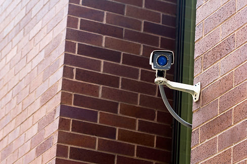 A surveillance camera mounted on a red brick wall, facing outward