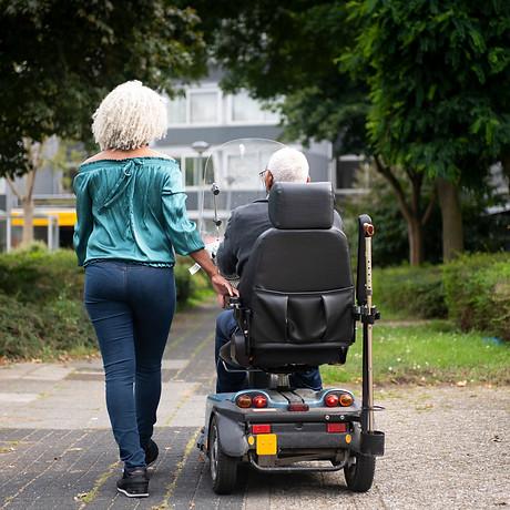 62 year old daughter walking next to 91 year old father in mobility scooter