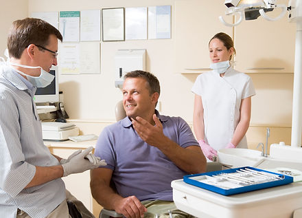 Dentist and assistant in exam room with man in chair smiling