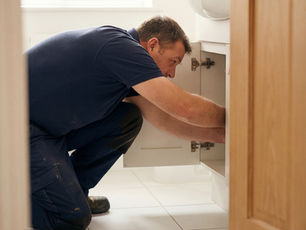 Technician repairs a leaking pipe under an office kitchen sink — maintenance request form