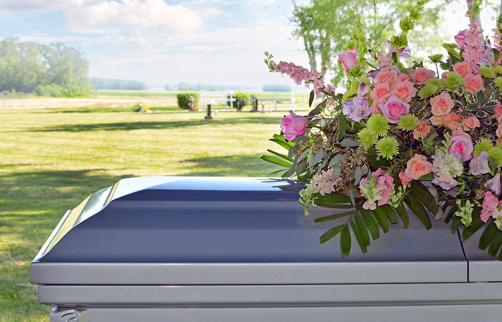 Closeup of a casket and floral funeral spray with a rural scene in the distance