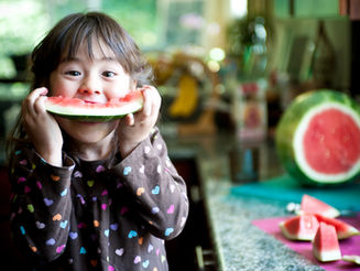 A child delightfully enjoys a slice of watermelon in the kitchen, capturing the essence of a joyful summer moment with bright eyes and a playful smile.