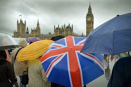 Tourist umbrellas huddle (one with a British Flag) near the Houses of Parliament in gloomy London