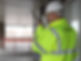 A security officer in a bright yellow jacket and helmet communicates via walkie-talkie on a covered walkway