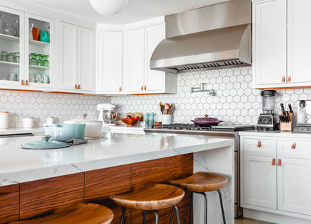 Modern white kitchen with stainless steel appliances and wooden bar stools.