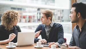 A trio of office workers sitting around a desk in discussion about a project.