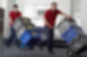 Two men wheeling crates on sack barrows through office area