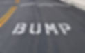 The word bump spelled out on the street before a speed bump, which is also know as a sleep