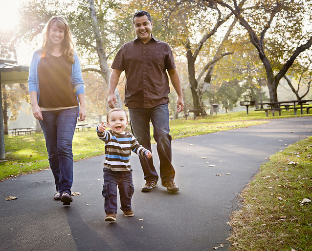 A family walking with their toddler in the park. Child is receiving speech therapy services through parent coaching. Speech therapist shares strategies with family so they can target child's speech and language goals in daily routines.